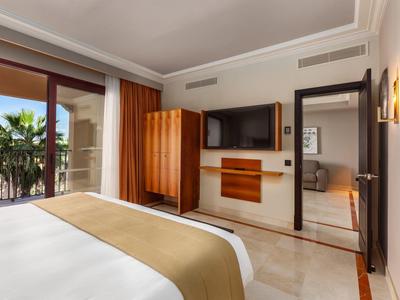 Helles Schlafzimmer mit Doppelbett, Holzschrank, Flachbildfernseher und Glasfenster zur Terrasse.