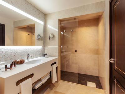 Modernes Badezimmer mit großer Glasdusche, hellen Fliesen und beleuchtetem Spiegel über dem Waschtisch.