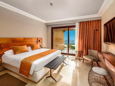 Modernes Hotelzimmer mit großem Bett, orangefarbenen Akzenten und Balkon mit Meerblick.
