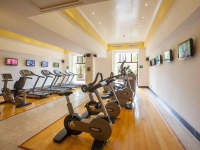 Heller Fitnessraum mit Fahrradergometern, Laufbändern, Spiegelwand und Holzboden.