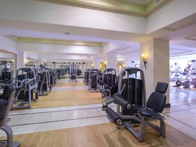 Großer heller Fitnessraum mit modernen Trainingsgeräten auf Holz- und Fliesenboden.