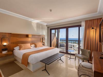 Modernes Hotelzimmer mit Doppelbett, Holzakzenten, Balkon und Blick auf das Meer bei Tageslicht.