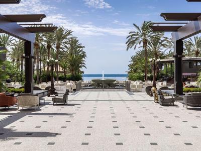 Große Terrasse mit Sitzbereichen, Palmen und Aussicht aufs blaue Meer unter blauem Himmel.