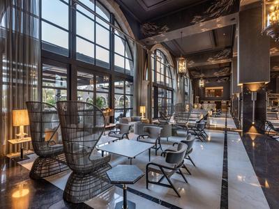 Elegante salón de hotel con grandes ventanales, sillas modernas y luz cálida.