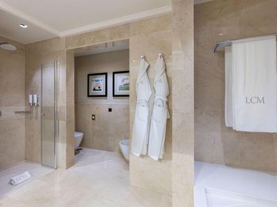 Helles Badezimmer mit Marmorwänden, begehbarer Dusche, Handtüchern und Bademänteln an der Wand.