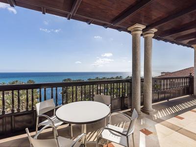 Balkon mit runden Tisch, Stühlen und Säulen, Blick auf Meer und blauen Himmel.