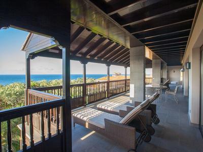 Großer Balkon mit Holzdach, Sitzbank und Blick auf das blaue Meer und den klaren Himmel.
