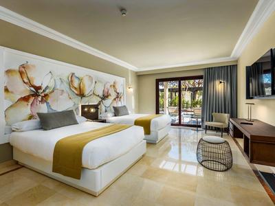 Helles Hotelzimmer mit zwei Doppelbetten, großer Blumenwanddekoration und Balkon mit Gartenblick.