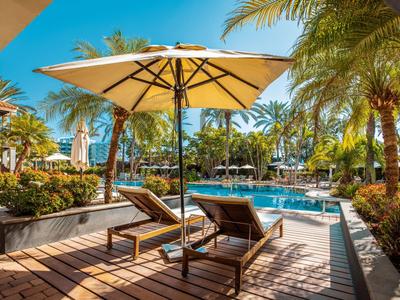 Sonnenschirme und Liegen am Pool mit Palmen und blauem Himmel im Hintergrund.