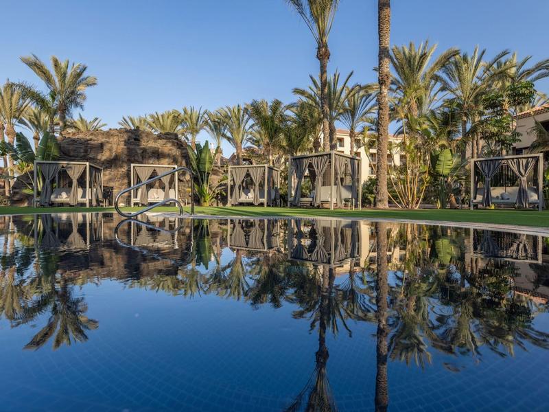 Modrý bazén s palmami a stinnými lehátky v slunném resortu.