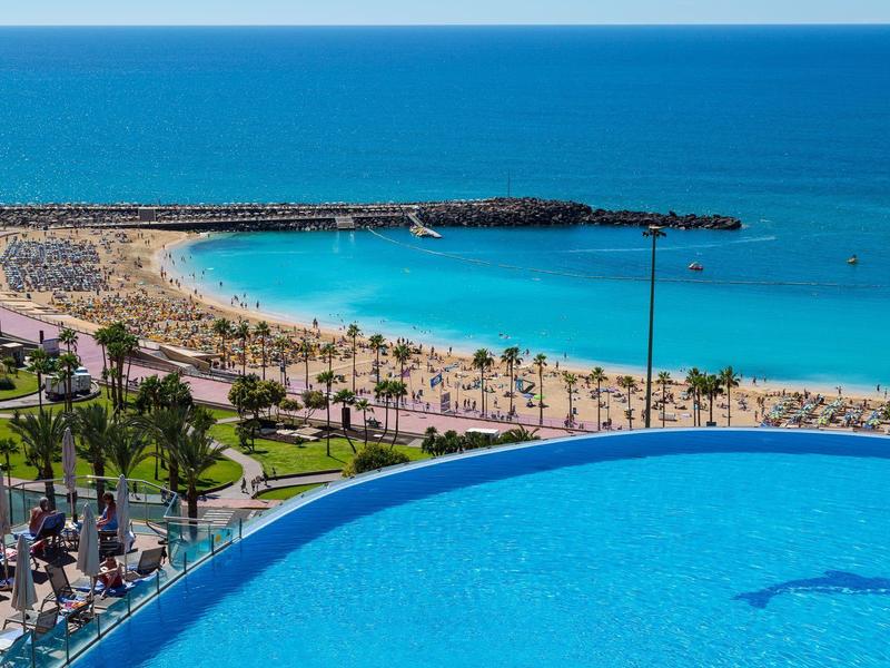 Pláž s deštníky a zakřivený mořský bazén s výhledem na oceán a písečnou pláž.