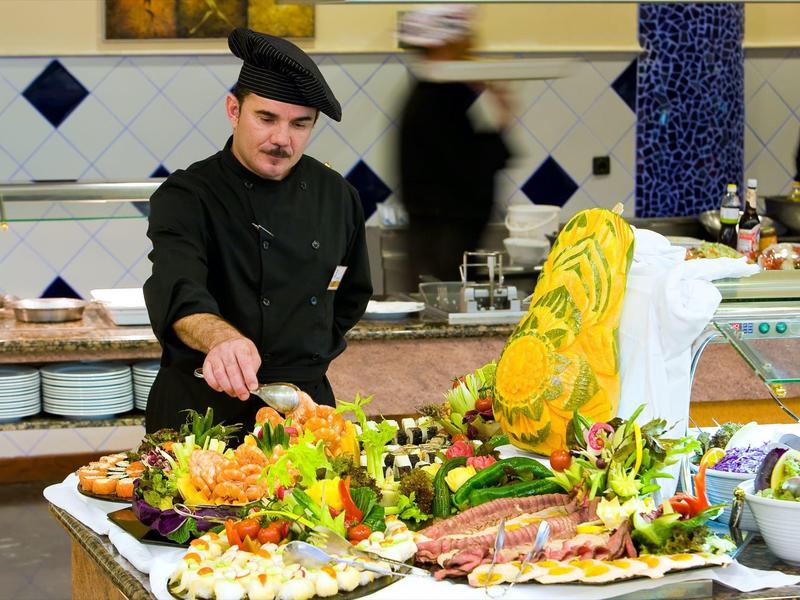 Šéfkuchař upravující barevný bufet z ovoce a zeleniny v jídelně.