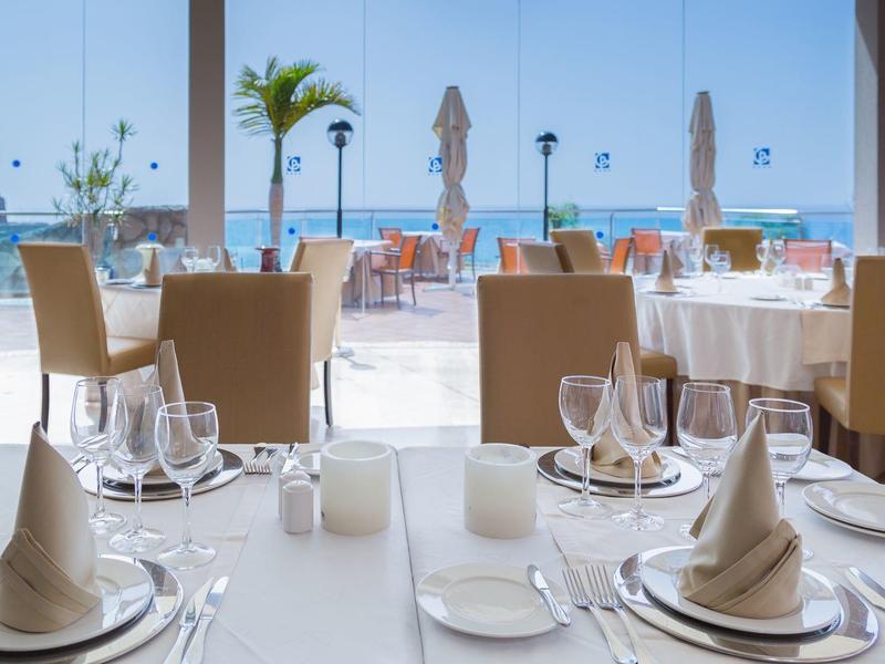 Elegantní uspořádání restaurace s bílými ubrusy a výhledem na palmy a moře.