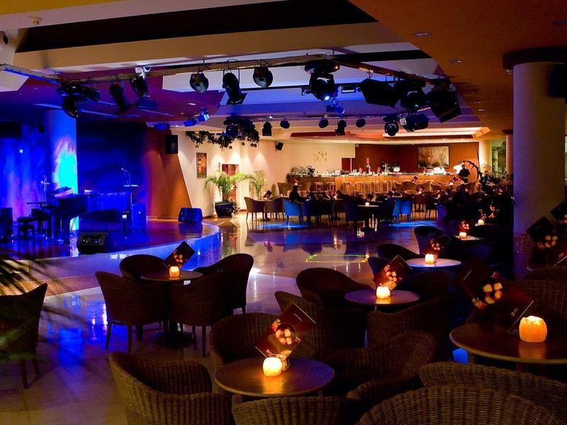 Příjemný bar a lounge s tlumeným osvětlením a svíčkami, jeviště s modrým osvětlením.