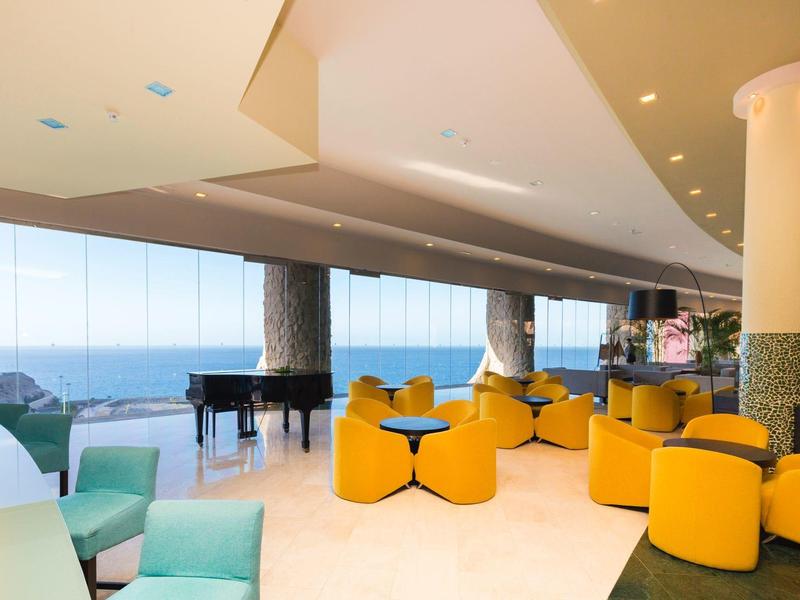 Světlý hotelový salonek se žlutými křesly, velkými okny a výhledem na oceán
