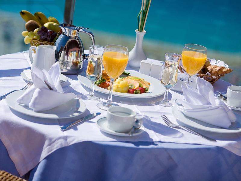 Stůl u oceánu připravený na snídani s bílým ubrusem, pomerančovým džusem a croissanty.