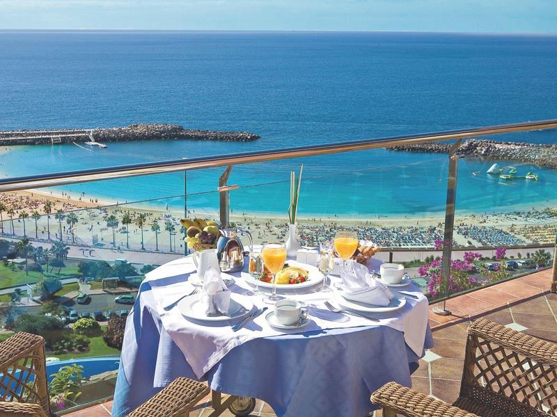 Stůl připravený na snídani na balkoně s výhledem na pláž a oceán.