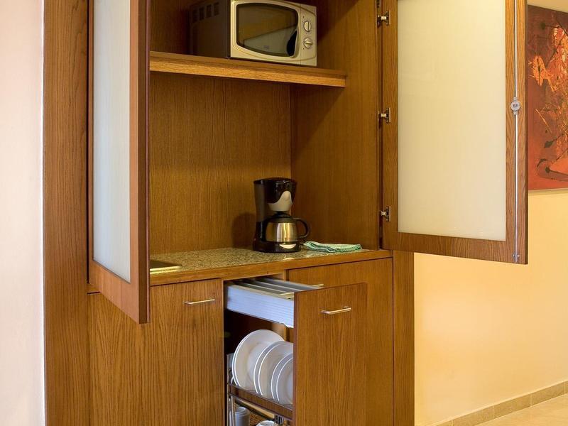 Dřevěná kuchyňka s mikrovlnnou troubou, kávovarem a policemi s talíři a ručníky.