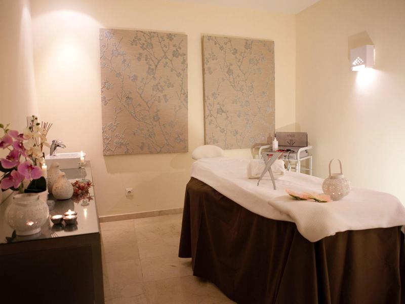 Pohodlná spa místnost s masážním stolem, jemným osvětlením, květinami a úhledně složenými ručníky.