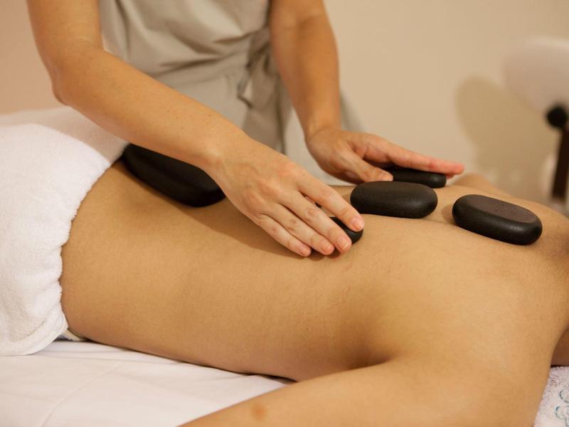 Osoba dostává masáž horkými kameny na zádech v lázeňském prostředí.