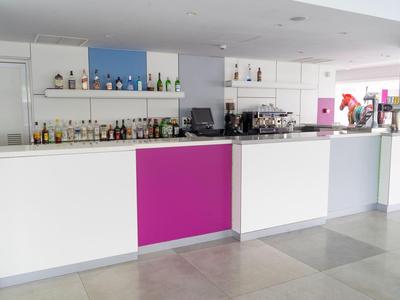 Moderní hotelový bar s bílým a růžovým pultem a různými lahvemi alkoholu.