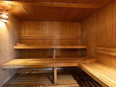 Dřevěná sauna s dvouúrovňovými lavicemi a teplým nástěnným osvětlením.