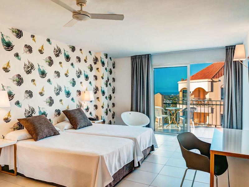 Chambre d'hôtel avec deux lits simples, mobilier moderne et balcon avec vue sur la mer.