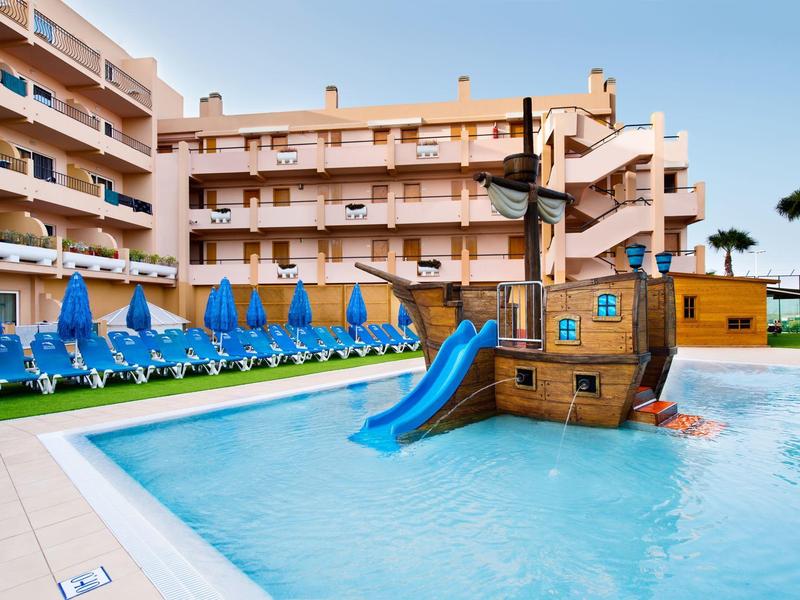 Piscine d'hôtel avec toboggan pour enfants en forme de bateau pirate et chaises longues bleues