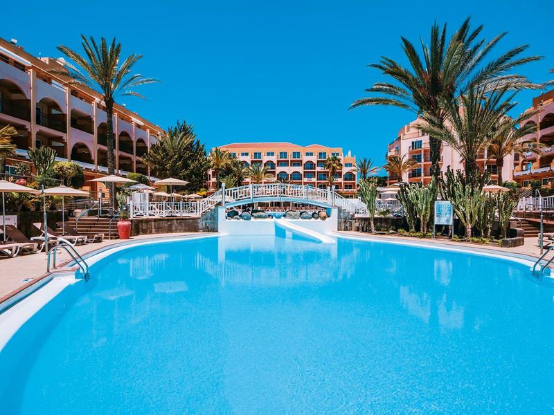 Grande piscine d'hôtel avec pont, palmiers et bâtiments de l'hôtel par temps ensoleillé
