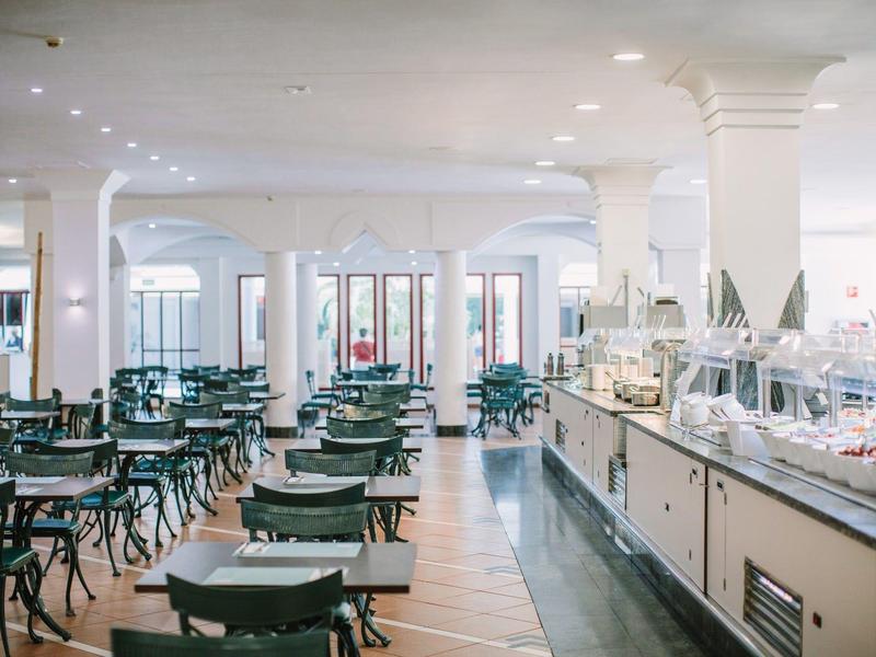 Restaurant lumineux et spacieux avec de nombreuses chaises vertes et un buffet.