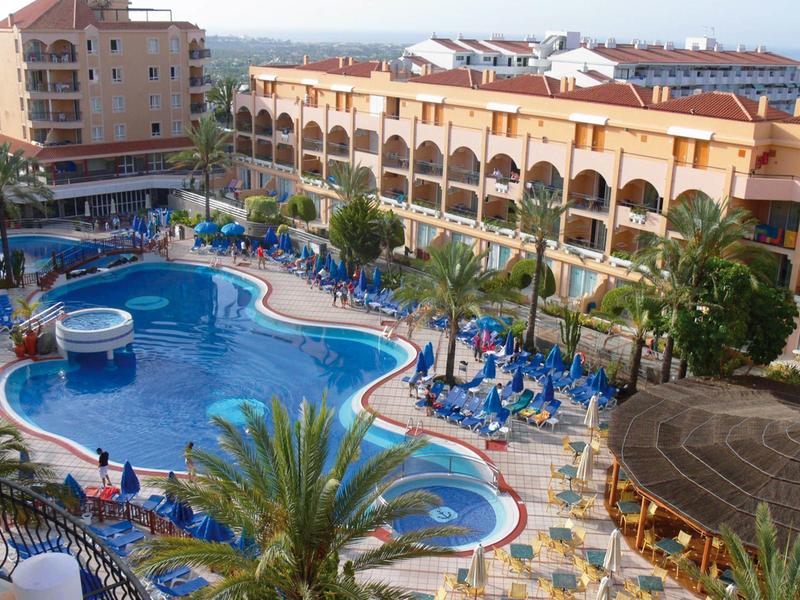 Grande piscine extérieure avec chaises longues et parasols à côté d'un bâtiment hôtelier à plusieurs étages.