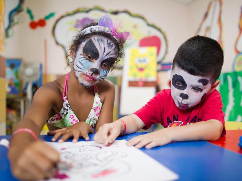 Deux enfants au visage peint colorient ensemble à une table dans une pièce colorée.