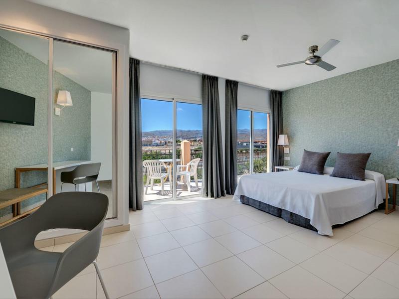 Chambre d'hôtel moderne avec lit double, bureau, balcon et vue sur la ville.