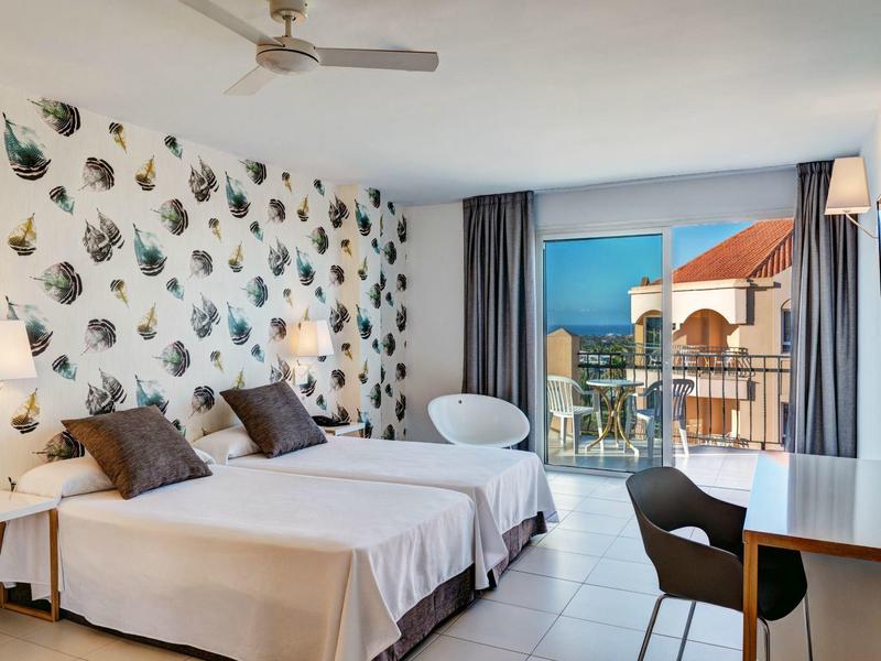 Chambre d'hôtel lumineuse avec deux lits simples, balcon et vue sur la mer.