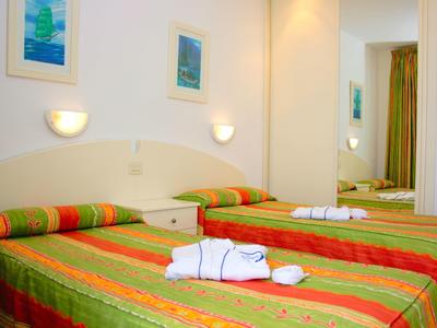 Zimmer mit zwei Betten, gestreifte bunte Bettwäsche, Handtücher und Wandbilder, Spiegel an der Wand.