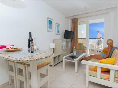 Camera d'hotel luminosa con angolo salotto, tavolo da pranzo e balcone con vista mare.