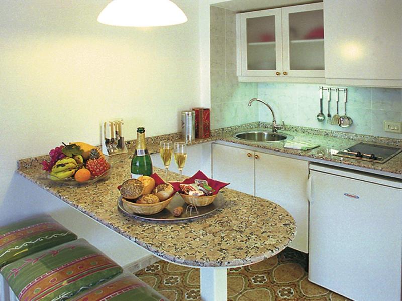 Petite cuisine avec plan de travail en granit, fruits, boissons et banc dans une chambre d'hôtel.