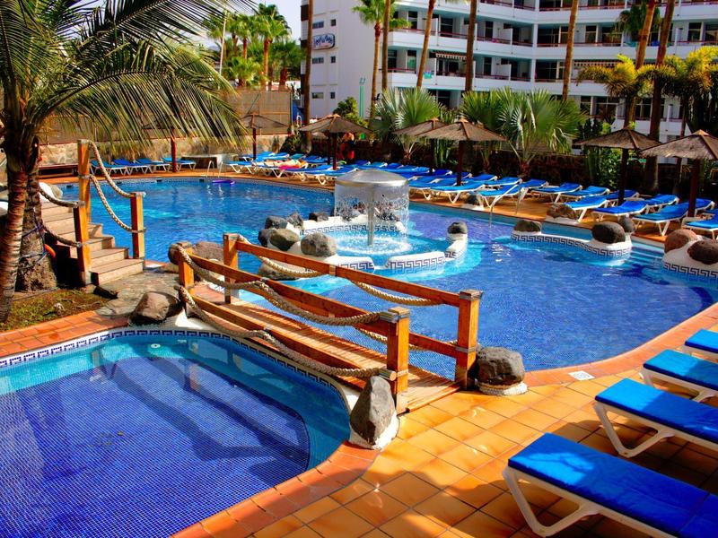 Grande piscine d'hôtel avec chaises longues et palmiers sous un ciel lumineux.