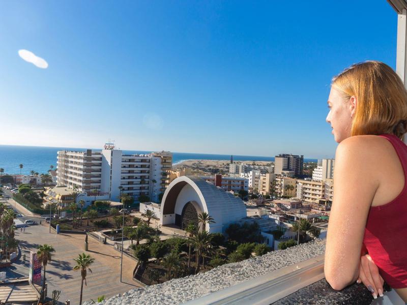 Femme regardant depuis un balcon la ville et la mer sous un ciel clair