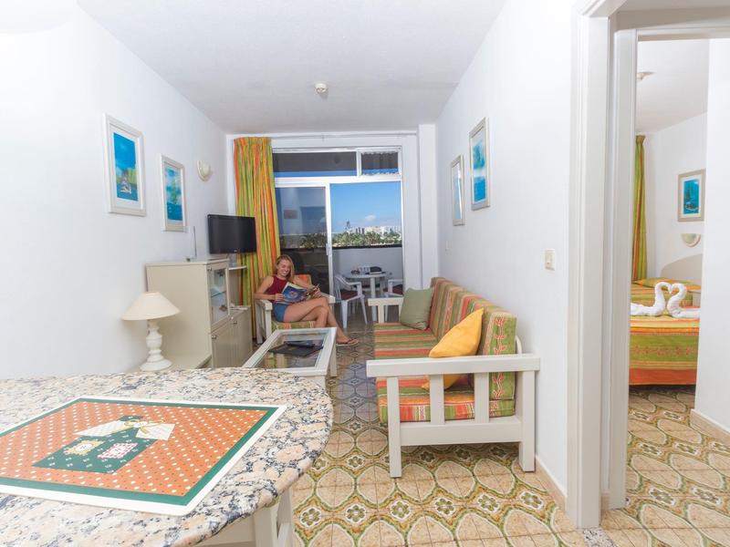Chambre d'hôtel lumineuse avec coin salon, table à manger et vue sur le balcon et la mer.