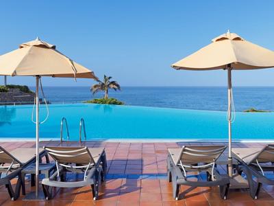 Infinity bazén s lehátky a slunečníky s výhledem na moře.