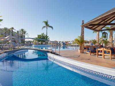 Hotelpool mit klarem Wasser, Sonnenschirmen und Palmen unter blauem Himmel.