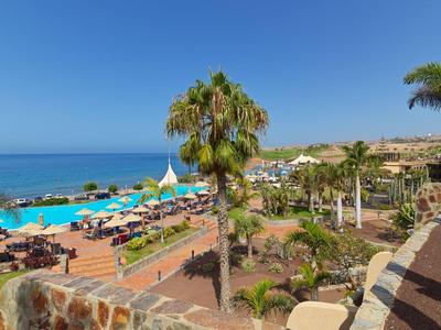 Přímořské letovisko s bazény, lehátky a palmami u moře pod jasnou oblohou.