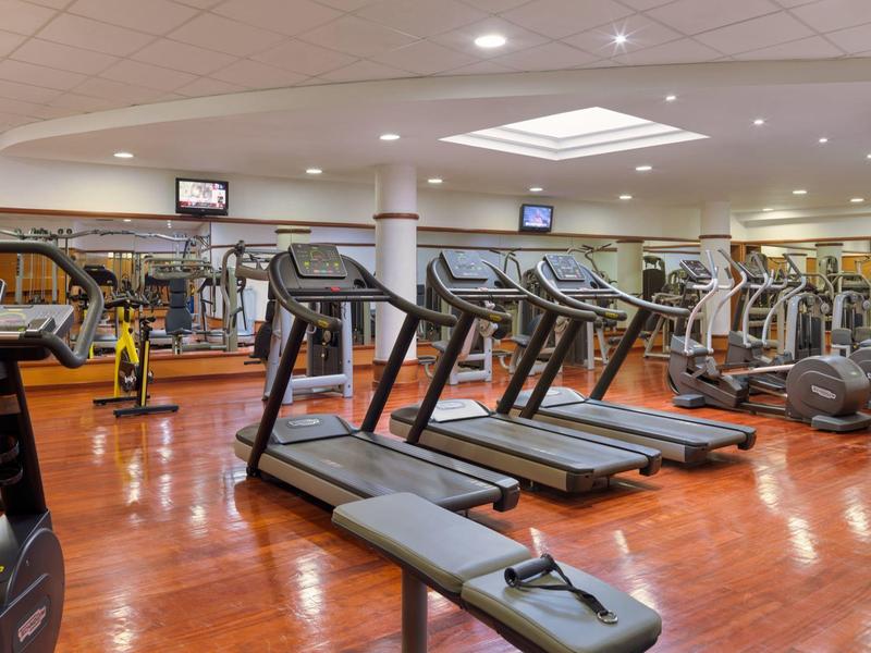 Moderner Fitnessraum mit Laufbändern, Rudergerät, Spinning-Bike und Spiegelwand bei heller Beleuchtung.