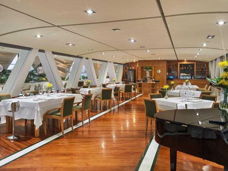 Eleganter Gastraum mit Holzboden, weißen Tischdecken und modernen Stühlen unter deckenlampen.