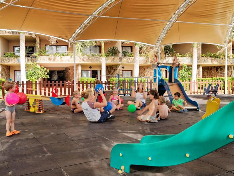 Spielplatz mit Kindern und Erwachsenen, farbige Bälle, Rutsche und überdachter Bereich.