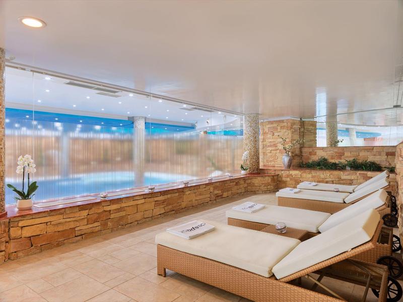 Moderner Innenpool mit Liegestühlen, Steinmauer, großen Fenstern und weißen Deckenbeleuchtungen.