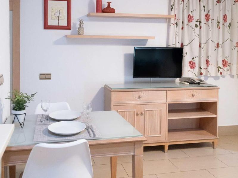 Nowoczesny pokój hotelowy z stołem jadalnym, telewizorem na szafce i jasnymi zasłonami.