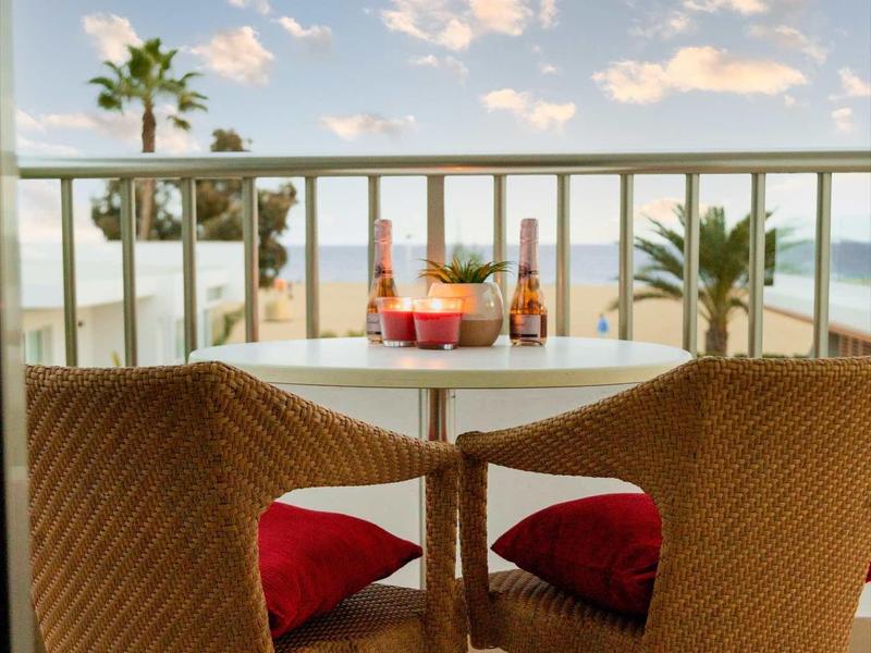Balkonowy stolik z dwoma krzesłami i czerwonymi poduszkami z widokiem na morze i palmy