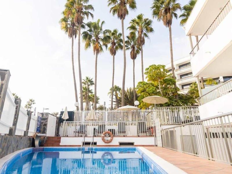 Basen z palmami i białym budynkiem w tle pod czystym niebem.